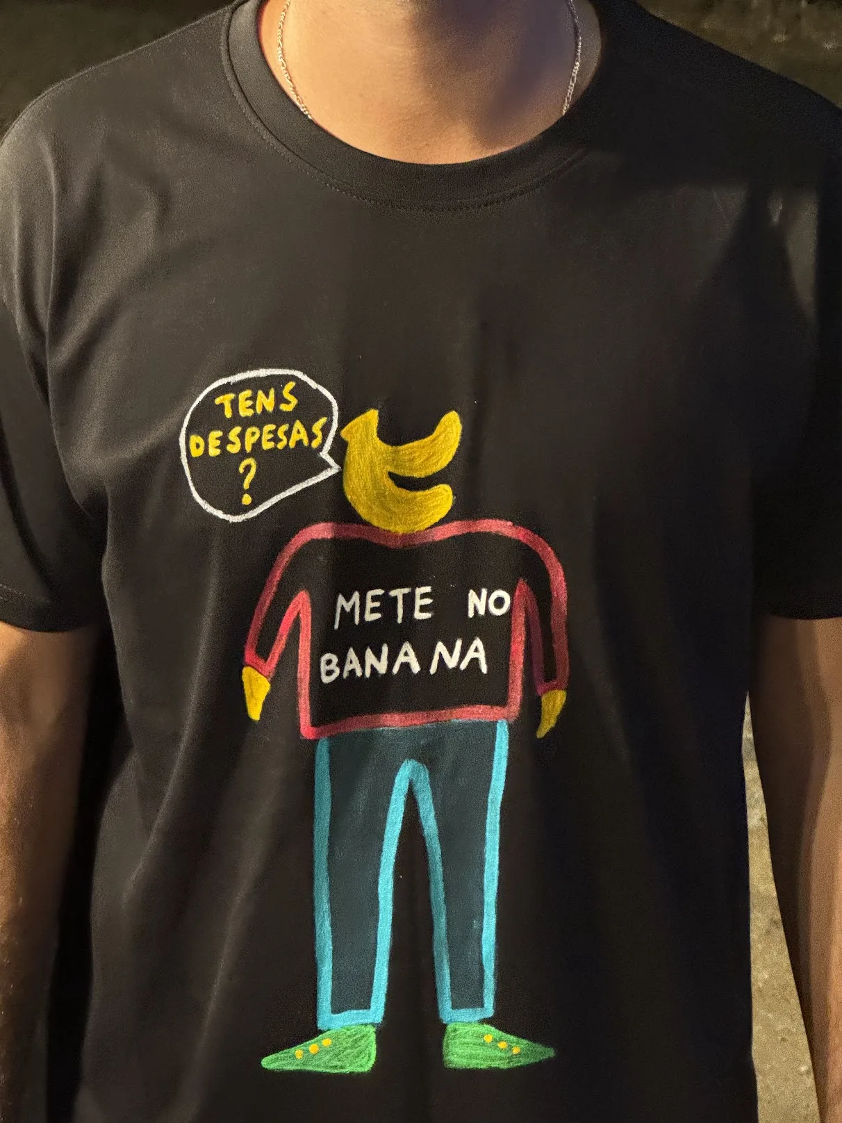 T-shirt preta pintada à mão com uma personagem banana e as frases «Tens despesas?» e «Mete no Banana»