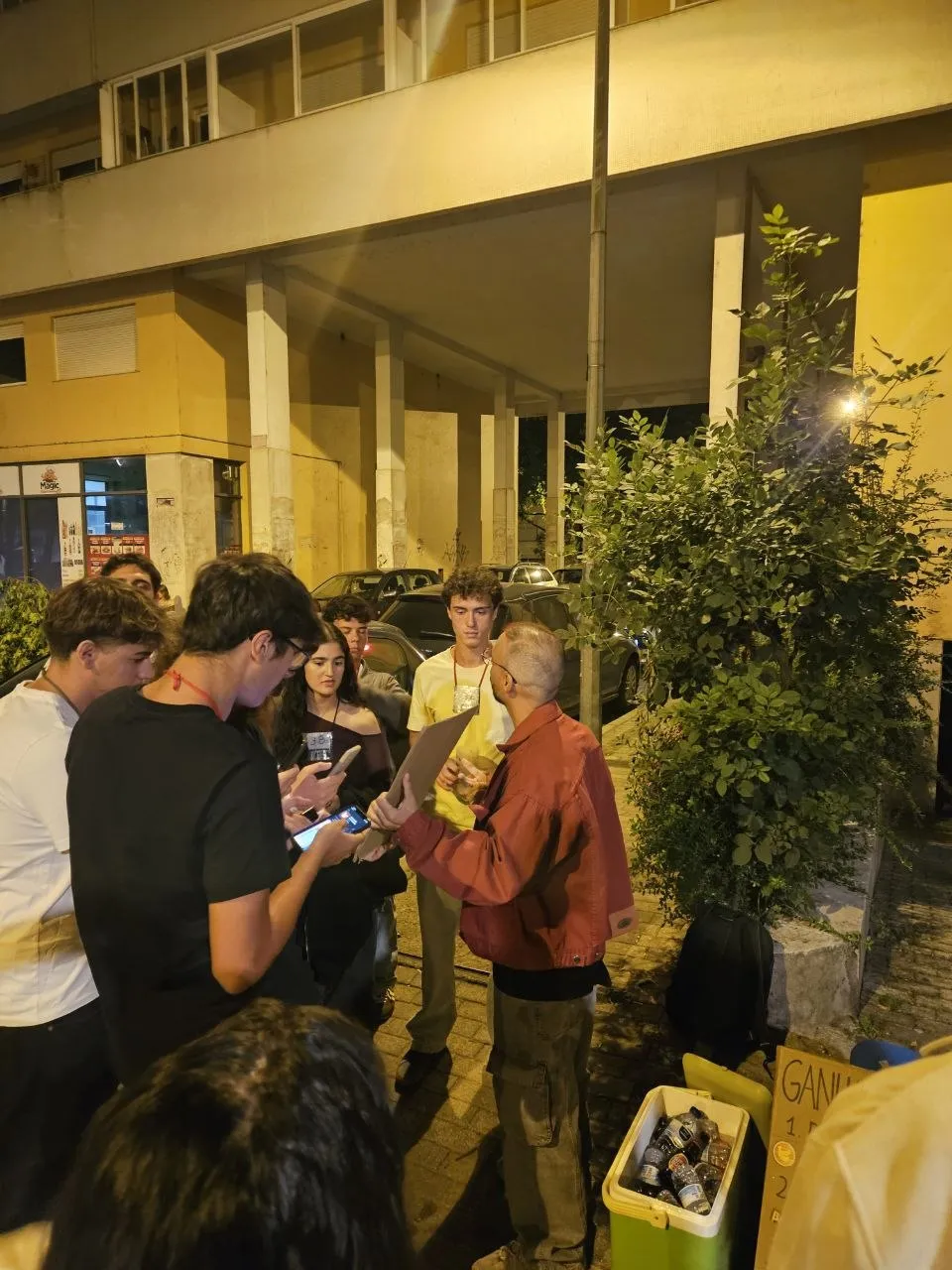 Conversación con un grupo de novatos, algunos con el móvil en la mano, junto al cartel y la nevera