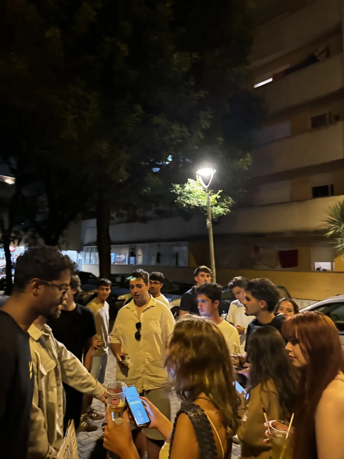Un grupo de estudiantes con vasos en la mano alrededor del equipo de BananaSplit, en una calle llena de noche