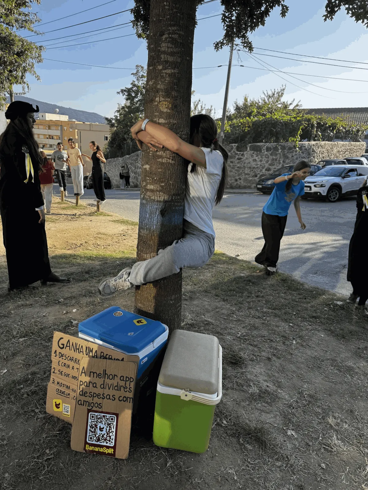 Una estudiante trepando a un árbol junto a las neveras y el cartel de BananaSplit durante una novatada