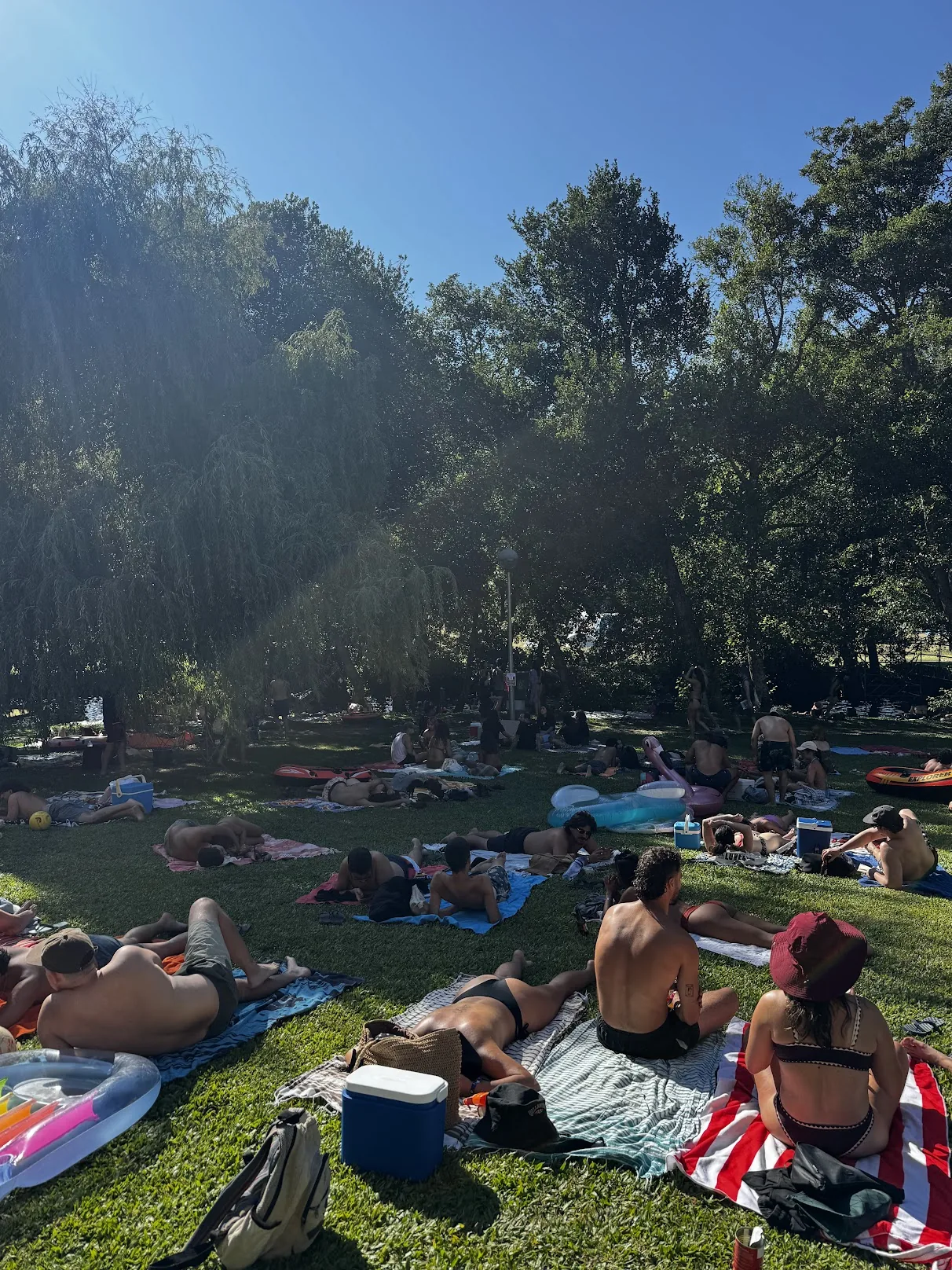 People on blankets and inflatables in the shade by the river