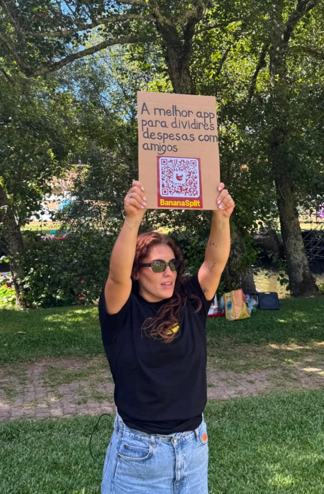 Mujer sostiene un cartel artesanal con QR de BananaSplit sobre su cabeza en un evento al aire libre